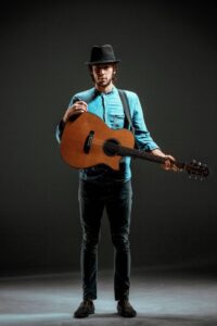 Cool guy with hat standing with guitar on dark studio background