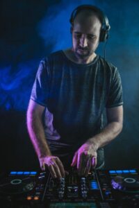 A vertical picture of a Male DJ under the blue lights and smoke in a studio